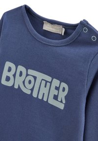 T-shirt en coton bleu marine avec un col rond, présentant un texte "BROTHER" en vert clair. Boutons-pression sur l'épaule pour un enfilage facile.