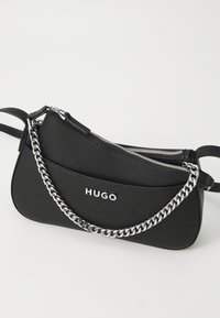 Schwarze Handtasche aus strukturiertem Material, mit Reißverschlussfächern und einem silbernen Kettenriemen. Das Logo "HUGO" ist deutlich auf der Vorderseite zu sehen.