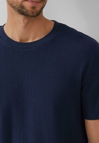 Donkerblauwe gestructureerde t-shirt met korte mouwen, voorzien van een ribpatroon en een ronde hals. Het materiaal lijkt zacht en ademend te zijn.