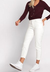 Jeans blancs, mi-hauts, avec poches latérales, coupe slim et chevilles retroussées. Associés à un haut boutonné bordeaux avec une texture côtelée.