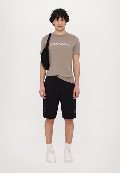 Light brown short-sleeve t-shirt with "EMPORIO ARMANI" text, paired with black shorts, white sneakers, and a black shoulder bag.