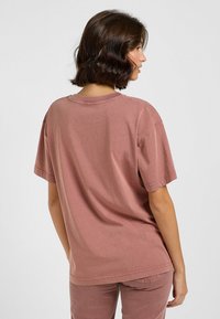 Staubrose Baumwoll-T-Shirt mit lockerer Passform, kurzen Ärmeln und einem runden Ausschnitt. Verfügt über sichtbare Nähte und einen leicht abgerundeten Saum.