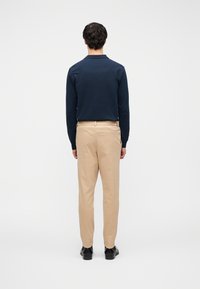 Μπλε σκούρο πόλο με μακριά μανίκια σε συνδυασμό με μπεζ παντελόνι, εφαρμοστό σχέδιο, λεία υφή, κανονικός γιακάς και παπούτσια που δεν φαίνονται από την πίσω όψη.