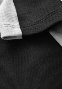 Černý a šedý textil s texturovaným povrchem. Má sklopený límec a kontrastní šedý pruh podél okraje.