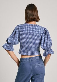 Modrý vzorovaný crop top s puff rukávmi a okrúhlym výstrihom, ktorý má biely diamantový vzor. Spárovaný s modrými nohavicami s vysokým pásom.