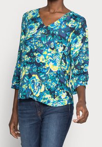 Blumenbluse in Marineblau mit lebendigen blauen, gelben und grünen Mustern. Verfügt über einen V-Ausschnitt und Dreiviertelärmel mit lockerer Passform.