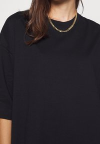 T-shirt en coton noir avec une coupe décontractée, des manches courtes et un col rond, associé à un collier en chaîne dorée.