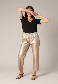 T-shirt noir à col en V avec un motif subtil, associé à un pantalon élastique doré métallisé. Le modèle se tient debout dans des talons noirs à lanières.