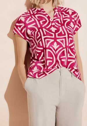 Kurzärmeliges Oberteil in leuchtendem Pink mit weißem geometrischem Muster und Ausschnittkragen, gefertigt aus leichtem Stoff, kombiniert mit hellgrauen Hosen.
