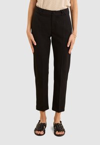 Pantalons noirs ajustés à taille haute, avec un détail de nœud décoratif à la taille et une coupe slim et fuselée.