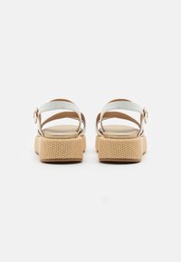 White sandals featuring a textured tan platform, adjustable ankle strap, and smooth footbed. Open design with padded interior.