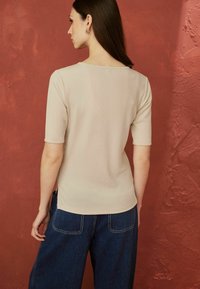 Beige ribbet top med korte ærmer og bred udskæring, parret med mørkeblå højtaljede jeans med baglommer.