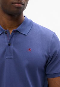 Polo blu con tessuto a texture, due bottoni al colletto e un piccolo logo rosso ricamato sul petto sinistro.