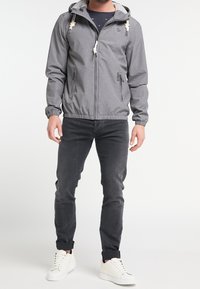 Harmaa hupullinen vetoketjutakki, jossa on kuminauhakiinnitteiset hihansuut, kaksi etutaskua vetoketjulla ja kiristysnyörit. Päällä tummat farkut ja valkoiset tennarit.