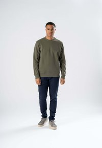 Oliven grøn sweatshirt med rund halsudskæring, struktureret stof, ribbede manchetter og kant, parret med marineblå bukser og grå sneakers.
