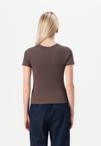 Brun randig t-shirt med korta ärmar och rund halsringning, ihop med mörkblå denimbyxor. Enkelt mönster, åtsittande silhuett.