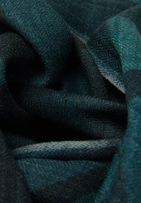 Tissu en tricot aux teintes bleu sarcelle profond et noir, mettant en valeur un motif en chevrons avec une texture douce et des nuances variées dans les plis.