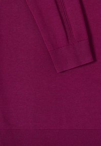 Gros plan sur un pull à manches longues magenta montrant un poignet et un ourlet côtelés texturés sur un tissu en maille lisse.