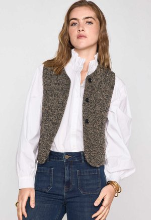 Brown herringbone vest with a fitted design, featuring black buttons, worn over a white ruffled shirt and dark denim pants.