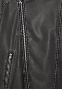 Section d'une veste en cuir noire montrant le zip principal vertical et le zip de poche diagonal avec des coutures.