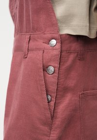 Κοντινό πλάνο ροζ φούστας από κοτλέ με ασημένια κουμπώματα και μπεζ κορυφή που είναι φορεμένη μέσα στη μέση.