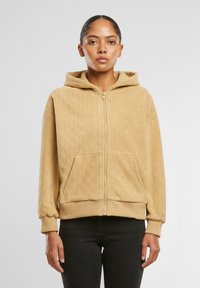 Hanorac zip-up bej cu model checker texturat, având o glugă spațioasă, două buzunare frontale și manșete și tiv cu dungi.