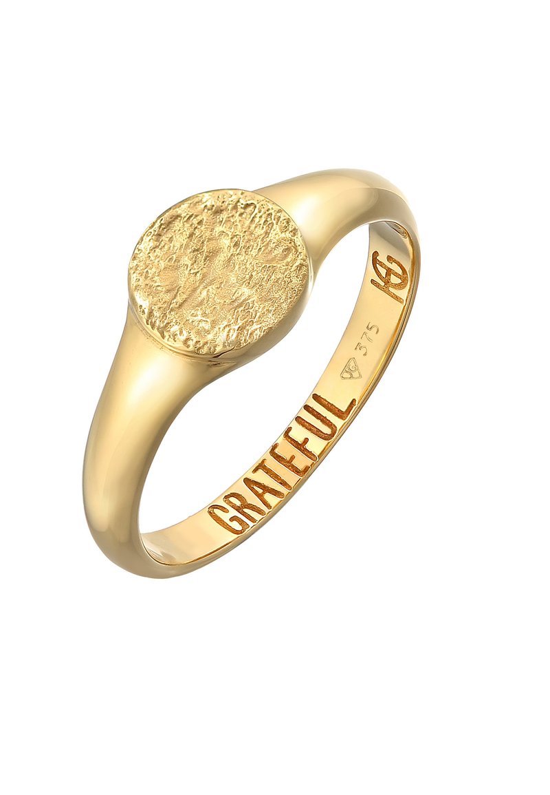 Guldring med en texturerad cirkulär yta, med ordet "TACKSAM" ingraverat inuti bandet. Materialet är markerat med 375.