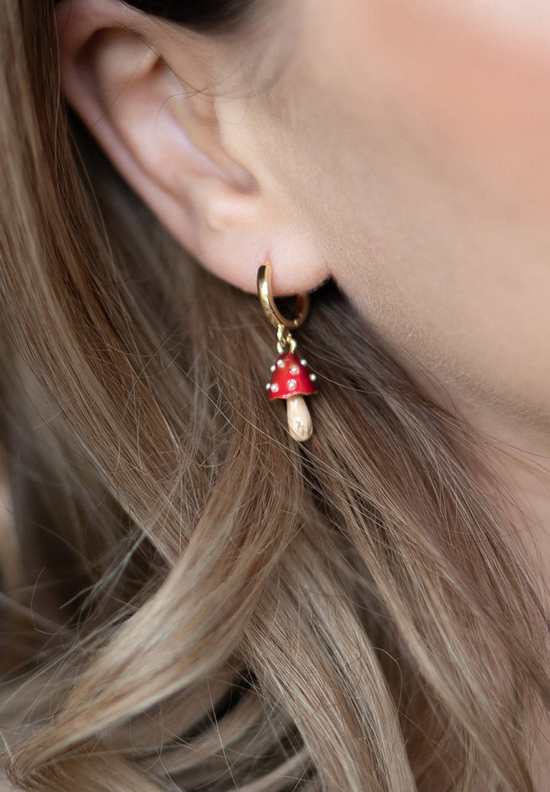 Gold hoop earring with a dangling red mushroom charm, featuring a white spotted cap and a beige stem, textured and playful design.