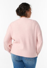 Gaiši rozā ribots džemperis ar garām piedurknēm un apaļu kakla izgriezumu, ar brīvu piegriezumu un teksturētu audumu. Kombinēts ar zilām džinsa biksēm.