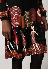 Jupe noire avec des imprimés colorés de femmes stylisées tenant de grands sucettes spirales, entourées de formes rondes multicolores à l'ourlet.