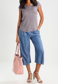 Grå mönstrad kortärmad topp, blå vida byxor, ljusrosa tote-väska och grå klacksandaler med vristremmar.