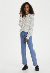 Vit långärmad blus med svarta och rosa prickar, avslappnad passform, knäppning vid halsen. Matchad med ljusblå raka jeans och svarta sneakers.