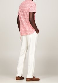 Kurzarm-Pinkhemd mit weißem Palmenmuster, kombiniert mit weißen Hosen und braunen Slippern. Glatte Textur und lässige Passform.