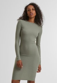 Abito a maniche lunghe a coste di colore verde spento, silhouette aderente, lunghezza a metà coscia, scollatura tonda, texture liscia e senza motivi o dettagli visibili.
