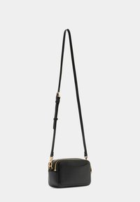 Borsa a tracolla in pelle nera con chiusura a zip, superficie testurizzata, tracolla regolabile e una semplice tasca frontale. Accenti in metallo di tonalità oro.