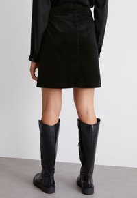 Jupe mini en velours côtelé noir avec une taille ajustée, des poches arrière et un motif texturé. Assortie à des bottes en cuir noir jusqu'au genou.