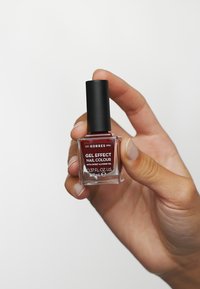 Vernis à ongles Gel Effect Korres dans un flacon en verre, teinte bourgogne profond, avec un capuchon noir. Le texte sur le flacon inclut les détails de la marque et du produit.