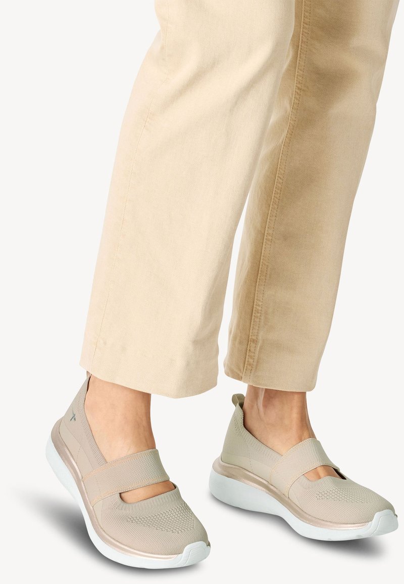 Pantofi sport bej cu partea superioară din plasă, curele elastice și o talpă albă din platformă. Pantofii au un vârf rotund și un design texturat.