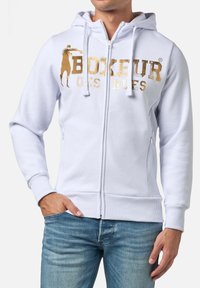 Felpa bianca con zip realizzata in tessuto liscio, caratterizzata da testo stampato in oro e un'illustrazione. Include cappuccio con coulisse e polsini a coste.