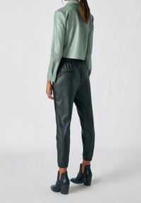 Veste cropped en faux cuir vert menthe avec manches longues, associée à un jogger en faux cuir noir doté d'une taille élastique et de poignets ajustés.