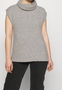 Pull sans manches gris clair à col roulé avec une texture côtelée et un ourlet allongé, fabriqué en matière tricotée douce.
