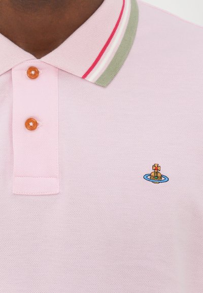Šviesiai rožinė polo marškinėliai su žaliai raudona dryžuota apykakle, keturiomis oranžinėmis sagomis ir išsiuvinėtu logotipu krūtinėje.