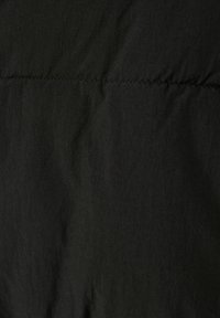 Svart nylon tyg med en något texturerad yta och synliga sömmar. Materialet verkar lättviktigt och motståndskraftigt mot skrynklor.