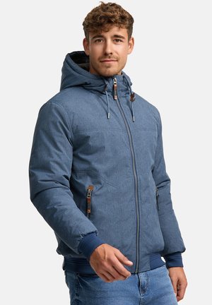 Chaqueta azul con capucha hecha de un tejido texturizado, con cremalleras en la parte frontal y puños acanalados. Presenta detalles en marrón en las cremalleras y cordones ajustables.