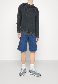 Pull en tricot côtelé gris foncé, short en jean bleu et baskets grises. Le pull a un col rond et une texture côtelée prononcée.