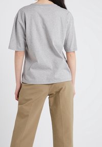 Camiseta de algodón gris con mangas cortas y cuello redondeado, combinada con pantalones de pierna ancha beige. La tela parece suave y casual.