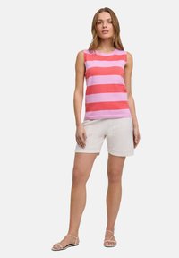 Mouwloze top met roze en koraalkleurige horizontale strepen, gecombineerd met witte, gestructureerde shorts. Sandalen met dunne banden maken de outfit compleet.