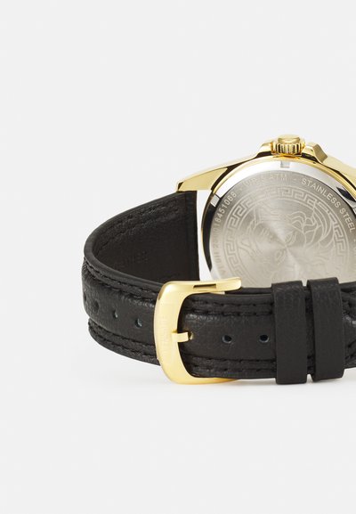 Fekete bőr óraszíj arany tónusú rozsdamentes acél tok. Strukturált felülettel és részletesen gravírozott hátsó résszel rendelkezik. Csattal záródik.