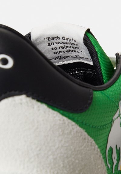 Πράσινο και μαύρο αθλητικό παπούτσι με σουέντ και υλικό με υφή. Διακριτικό απόσπασμα στο γλώσσα· διαθέτει λογότυπο και αντίθετο σχέδιο.
