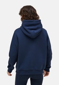 Marinblå huvtröja, tillverkad av mjukt tyg, med en avslappnad passform och ribbade muddärmar. Har en stor huva och inga synliga logotyper.